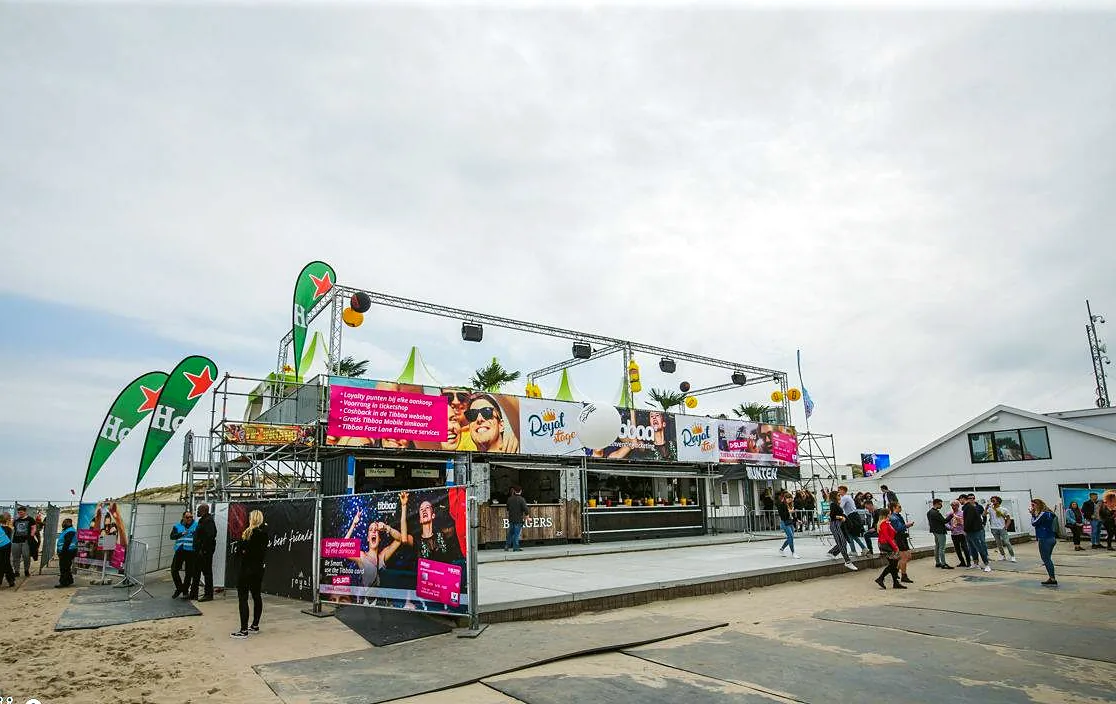 Buitenterrein van een strandfestival met vlaggen en bezoekers